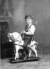 Little boy sitting on a rocking horse, 1910s, Boy in traditional clothing riding a wooden rocking