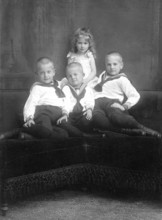 Three boys and a girl, 1930s, Three boys and a girl in traditional dress pose together on a sofa,