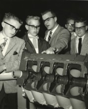 Pupil looks bored while teacher explains, 1950s, group of men examining a technical model. All