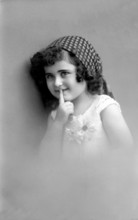 Girl is quiet, 1920s, Young girl with headscarf puts finger on lips and smiles mischievously,