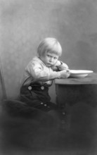 Child is angry while eating, 1920s, A boy sits thoughtfully at the table next to a bowl, Historical