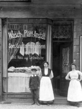 Washing and plating shop ca. 1915, woman and a boy in front of an antique shop with a window