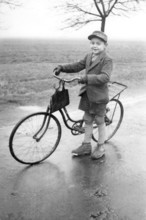 Boy with bicycle, 1920s, Boy standing with bicycle on a wet road in a rural environment, Historical