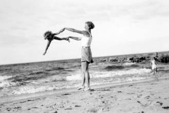 Woman with child on the beach, 1920s, Woman playfully turning a child on the beach while the sea