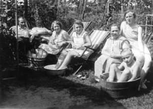 Hot summer in the garden, 1930s, people sitting in a garden and cooling off in containers filled