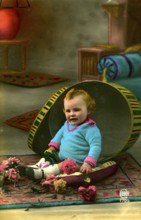 Child sitting in hatbox, 1905, A child sits in a half-opened, large Easter egg prop with flowers,