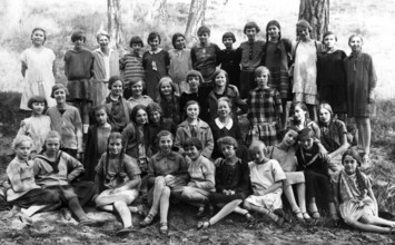 Girls class outing, 1930s, Large group of girls in school uniforms sitting outside in a wooded