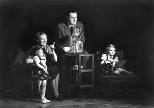 Family home cinema, 1930s, A family sits together in front of a film projector and watches with