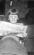 Girl's newspaper, 1920s, A child with glasses reads a newspaper with interest, sitting comfortably