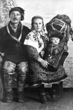 Sami in traditional dress with baby, 1930s, A traditionally dressed couple with a baby swaddled in