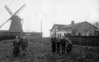 Farming family in a field with a windmill in the background, 1930s, Family standing on a farm near