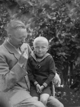 Father warns cheeky son, 1930s, A father lovingly holds his son in the garden, both in elegant