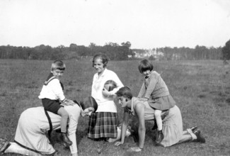 Two children riding on the backs of their mothers, 1930s, Children playing in the meadow with two