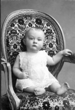 Baby sitting in armchair, 1911, A baby in a pretty, patterned armchair, looking attentively,