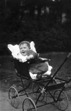 Laughing child in pram, 1910, A cheerful toddler in an antique pram in a park, Historical photo