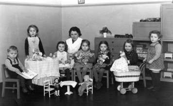Kindergarten group toys, 1930s, children with woman in the room, playing with dolls and toys at a
