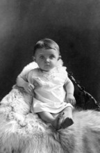 Baby sitting on polar bear fur, 1910, A baby sits on a fur, looking directly into the camera,