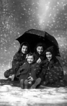 4 children in the snow, 1930s, A family sits under an umbrella in the snow for a group portrait,
