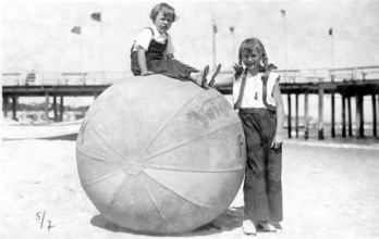 Big ball with 2 children, 1920, Two children on the beach, one sitting on a big ball, both smiling