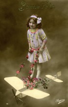 Girl with aeroplane, 1910, Girl in a purple dress posing with a toy aeroplane and flowers,