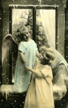 2 children as angels, 1920, Two children dressed as angels dancing in front of a decorated window,