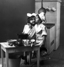 Boy kissing girl in kitchen, 1920, Two children in a kitchen setting with pots and crockery, one
