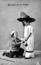 Boy kneeling in front of girl, 1910, A boy with flowers kneeling in front of a girl in a big hat,