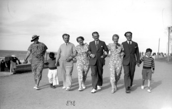 Family outing on the beach promenade, 1930s, A group of people stroll along the beach in elegant