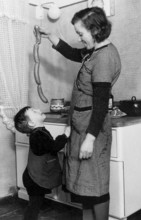 Mother feeding sausages to her son, 1930s, A woman shows sausages to a happy child in a cosy