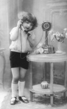 Child on the telephone, 1920s, A girl speaks into an old telephone, flowers on the table,