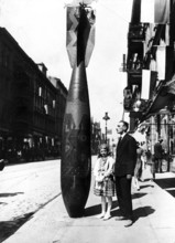Father and child next to bombs, 1940s, A man and a girl stand on the street next to a large bomb as