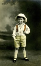 Boy with hat, 1920s, A little boy wears a straw hat and stands smiling in nature, Historical photo