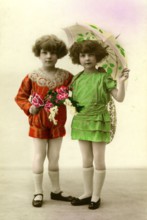 Two girls with umbrellas, 1930s, Twin girls in colourful clothes and umbrellas pose in a studio,