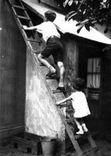 Two children on a ladder, 1920s, Two children climbing up a wooden ladder to a small building,