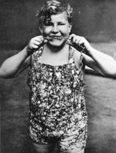 Child biting chains, 1910, A boy in a suit shows strength by pulling a chain and smiling,