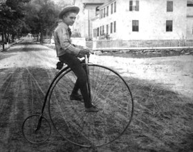 Boy on a penny-farthing, 1910s bicycle, Boy on an antique bicycle on a sandy street in a
