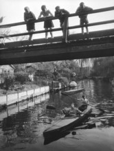 Four children on a bridge, 1930s, Children standing on a bridge while teenagers paddle underneath