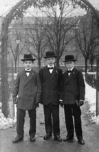 Young men, 1920s, Three boys in elegant clothes and hats stand under an arch on a snowy day,