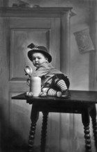 Baby traditional traditional costume beer mug, 1930s, child in traditional dress sitting on a table