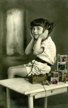 Child headphone radio, 1930s, girl with headphones sitting at a table with toys, historical photo