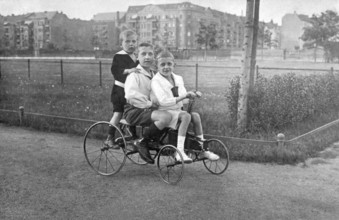 Three children on a historical bicycle, 1910s, Three children riding a tricycle on a cobbled
