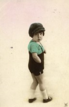 Little boy, 1920s, child with cap and green clothes in nostalgic pose in front of light background,