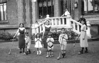 Family playing cricket, 1920s, group of children playing croquet in the garden in front of a large