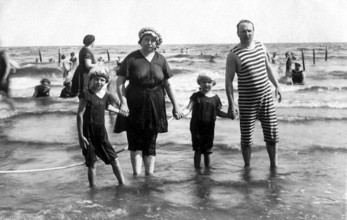 Family on the beach, 1920s, parents and children in the water, classic swimming costumes, relaxed