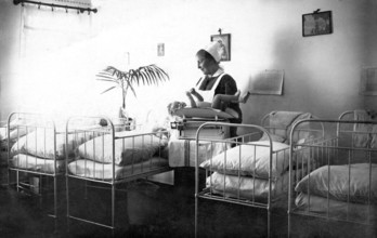 Beds Midwife cradling child, 1930s, Nurse caring for a baby in a room with several cots, Historical
