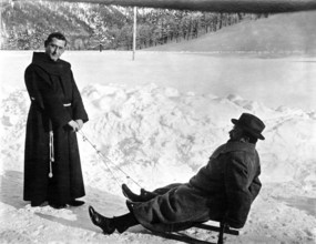 Monk and man in the snow, 1920s, Monk pulling a man in winter clothes on a sledge through the snow,