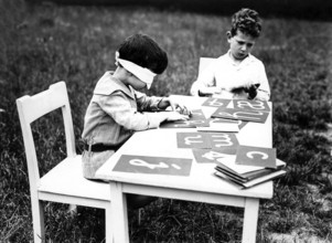 Blindfolded eyes, 1920s, Two boys busy themselves with flashcards while one is blindfolded,