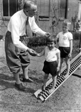 Children's physiotherapy, ca. 1925, A man helps two children on an outdoor slide in a black and