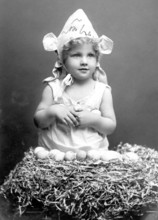 Child with Easter eggs, 1930s, Little girl in bunny costume sitting in a nest surrounded by eggs,