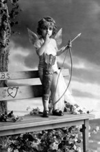 Little boy as Cupid, 1920s, A child dressed as Cupid, with wings and bow, standing on a bench,